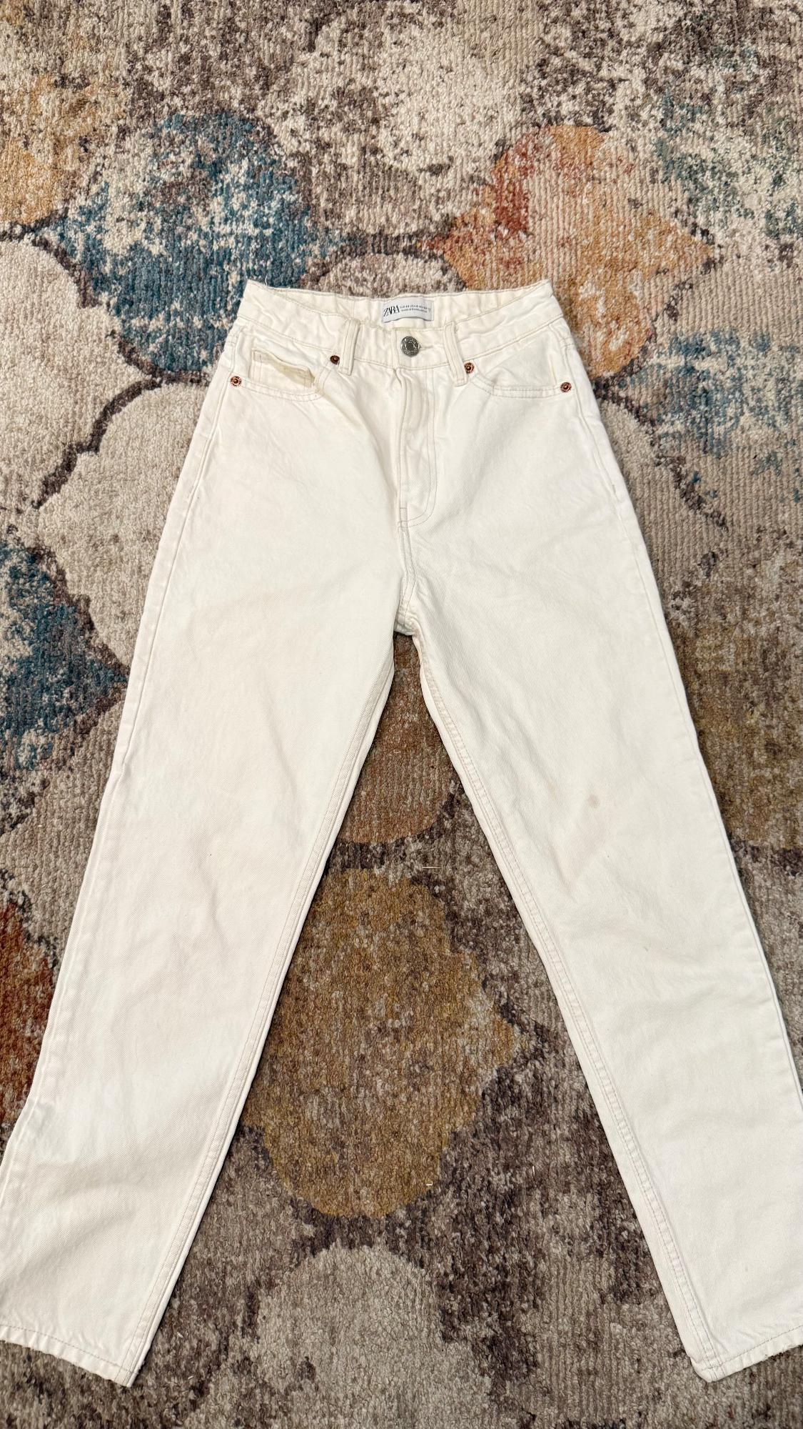 White denim pants on a rug with an abstract design in shades of brown, blue, and beige. Label visible at the waist.