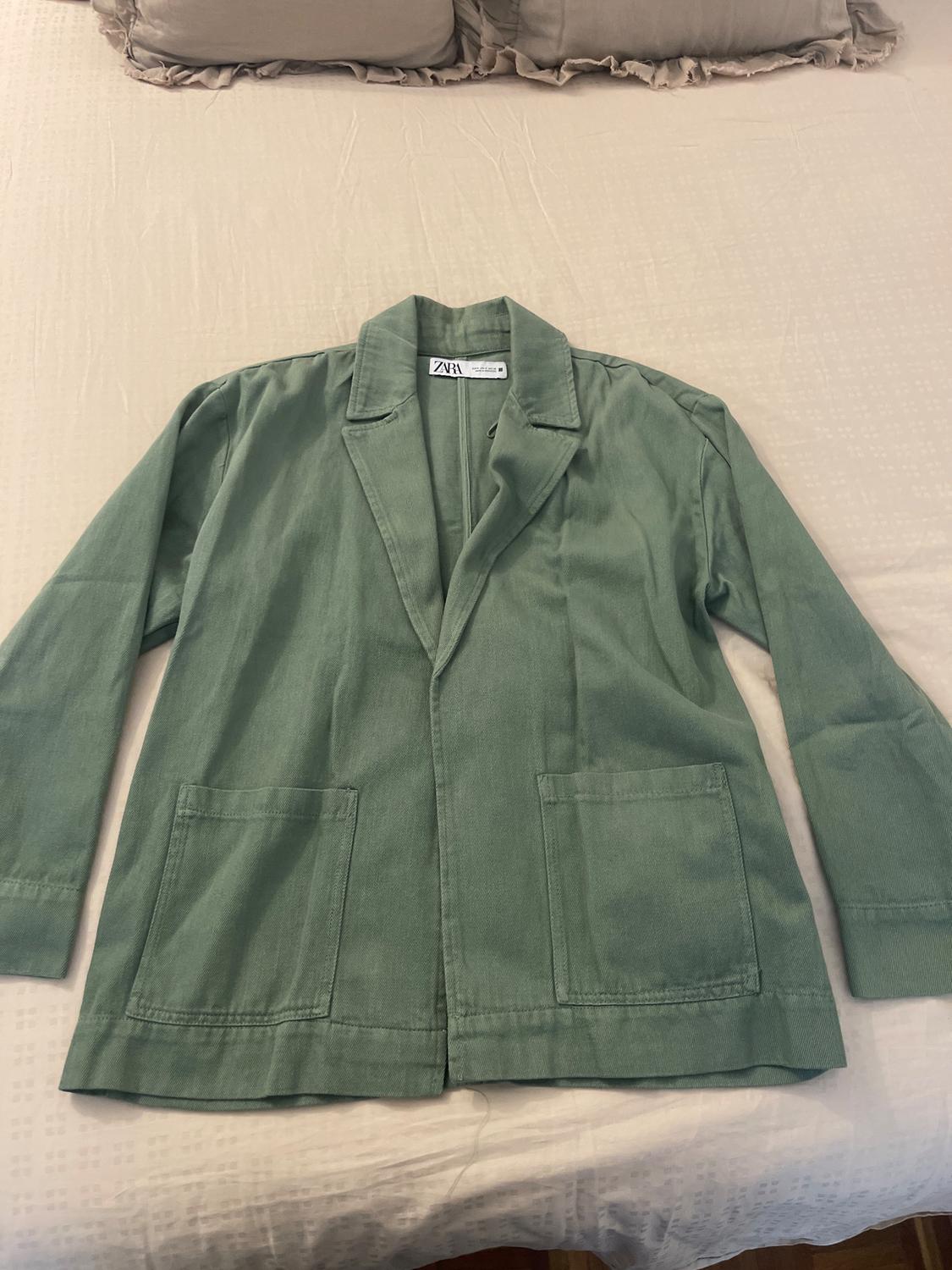 Long-sleeved green jacket with lapels and front pockets, on a beige bed. Visible label: "ZARA".