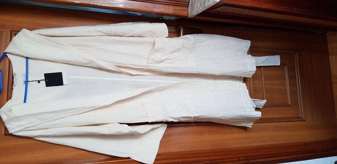 Beige coat hanging on a blue hanger over a wooden door. Black label visible on the coat collar.