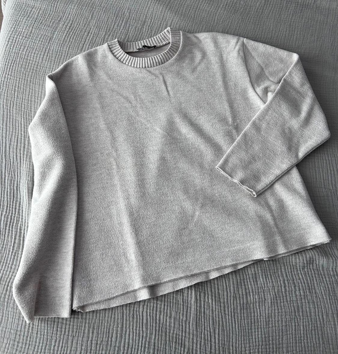 Light grey long-sleeved jumper on a textured grey bedspread.