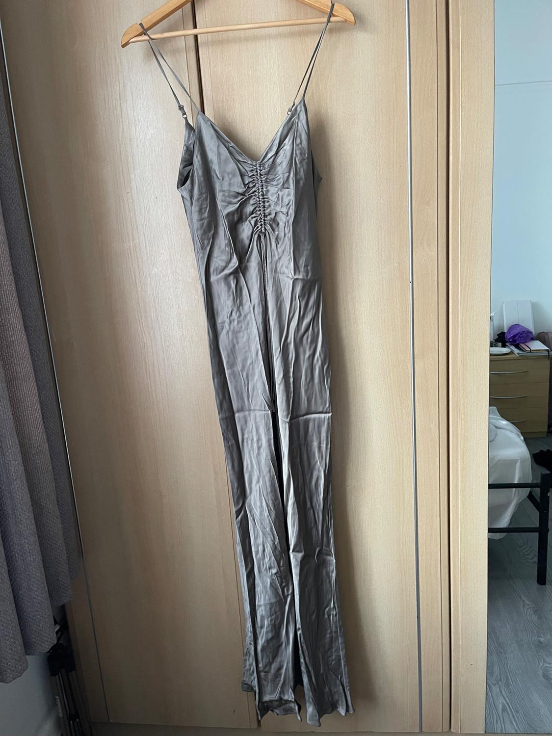 Grey maxi dress with spaghetti straps and ruched bust, hanging on a wooden hanger in front of a light wood wardrobe.