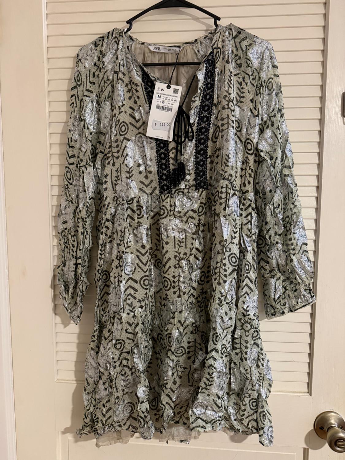 Printed dress hanging on a hanger, with a price tag of $119.00. White door background with blinds.