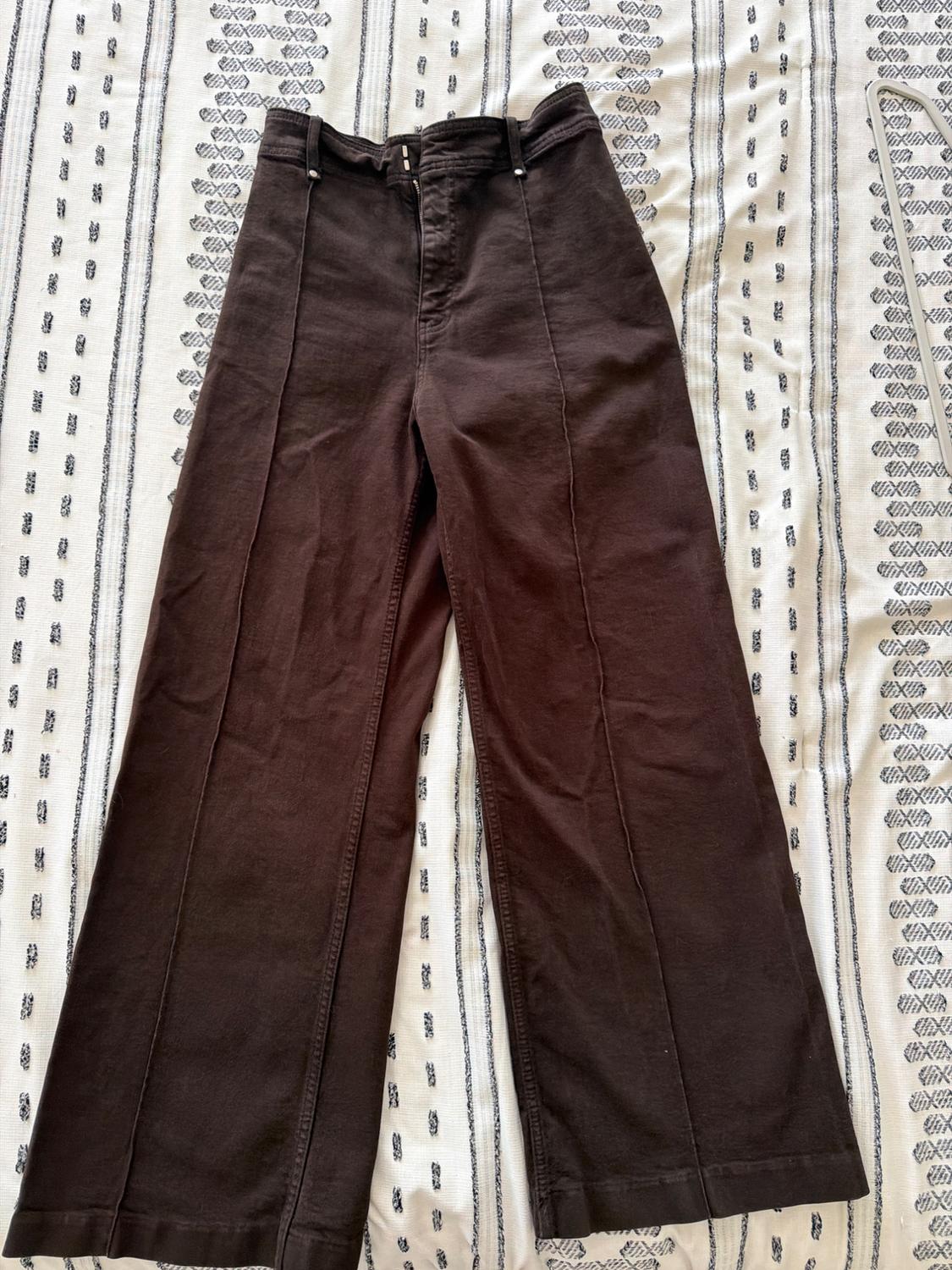 Dark brown wide-leg trousers with front seams, photographed flat on a white fabric with a black striped pattern.