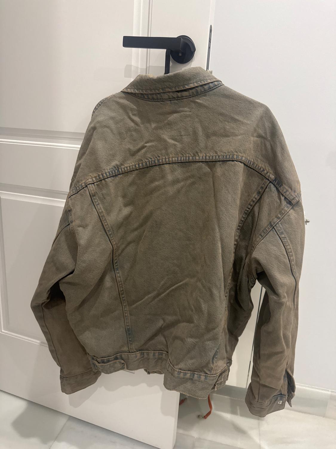 Πίσω όψη ενός καφέ casual μπουφάν κρεμασμένου στο μαύρο πόμολο μιας λευκής πόρτας, που αποπνέει μια χαλαρή ατμόσφαιρα.