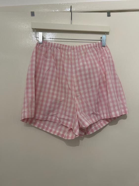 Pink and white gingham shorts hanging on a hanger over a white door.