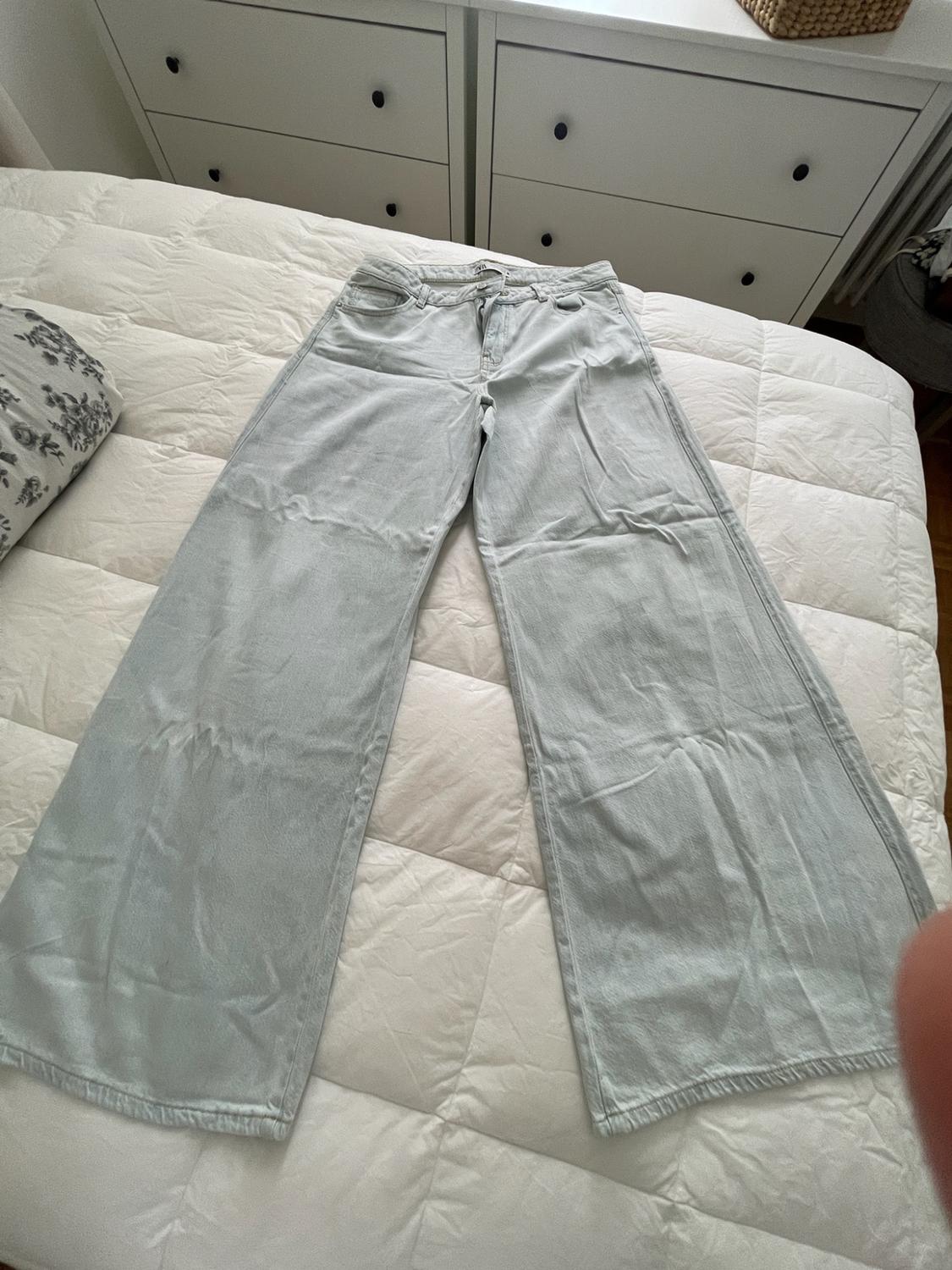 Light blue wide-leg jeans laid out on a bed with a white duvet. In the background, there is a white chest of drawers with black handles.