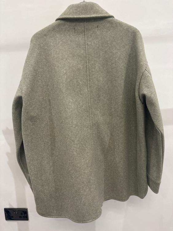 Light grey coat hanging on a white wall, viewed from behind. Soft-textured fabric and a straight cut with a classic collar.