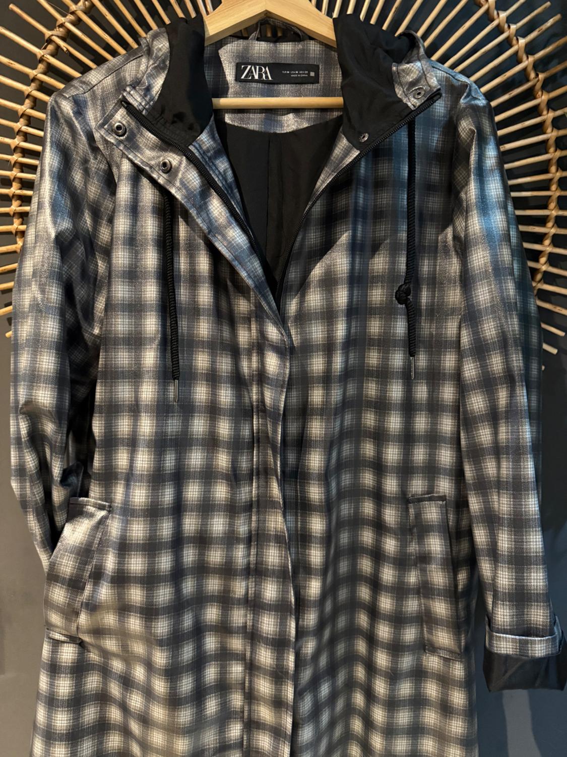Checked coat in grey and black tones hanging on a wooden hanger, with a black hood and visible Zara label.