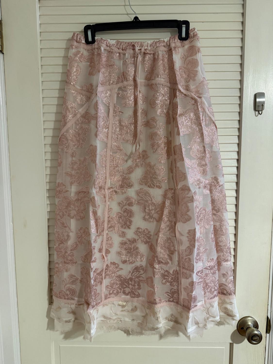 Long skirt hanging on a hanger, with a floral design in pink and white tones, against a white door in the background.