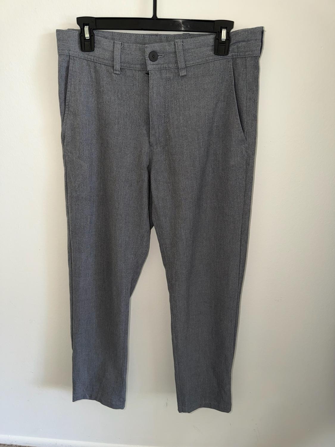 Casual gray pants with pockets and belt loops, hanging on a black hanger against a white wall.