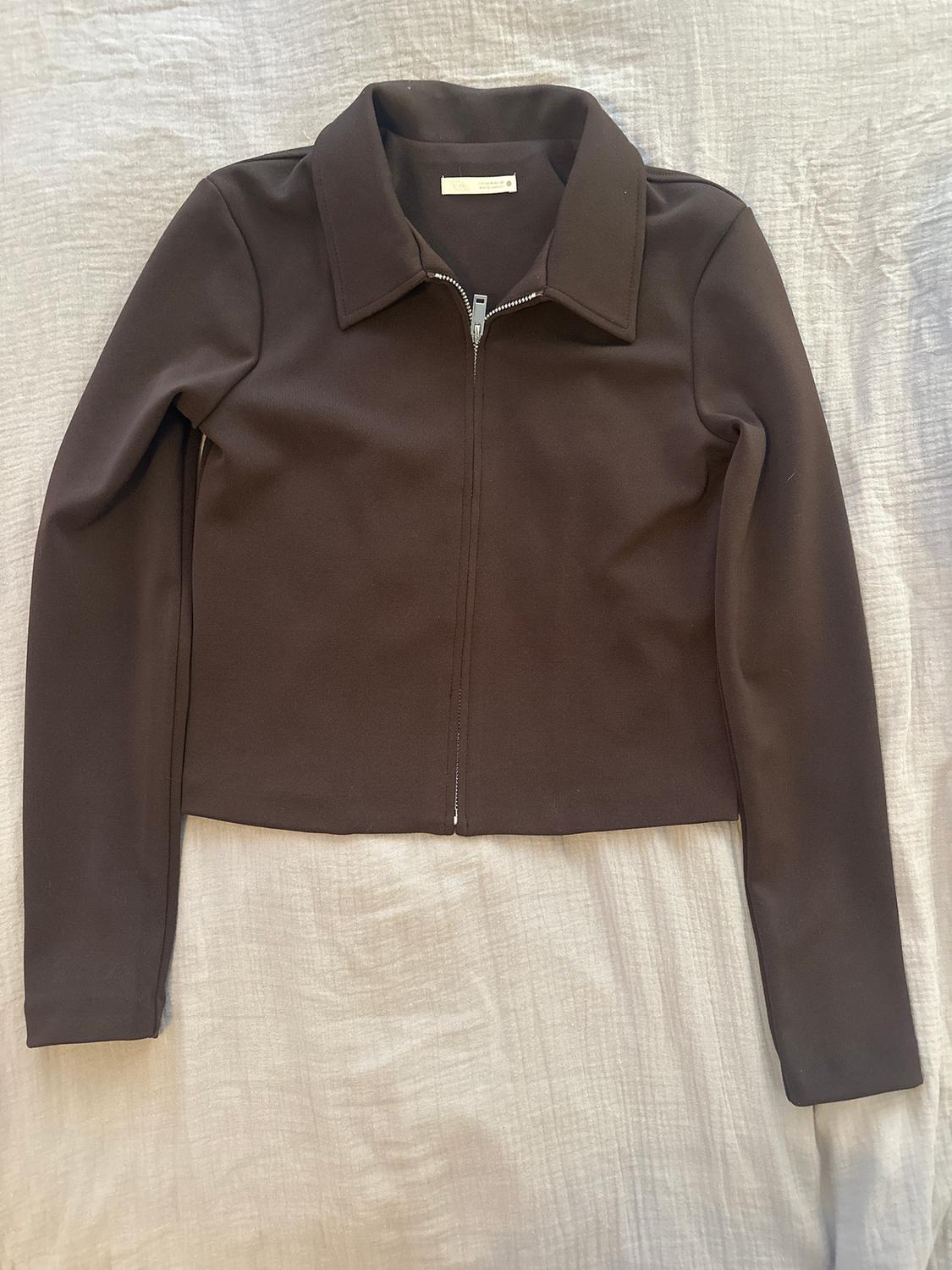 Brown long-sleeved jacket with a front zip and classic collar, on a light fabric surface.