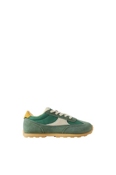 Green trainer with beige panels, yellow heel detail, light-coloured laces and a brown sole on a white background.