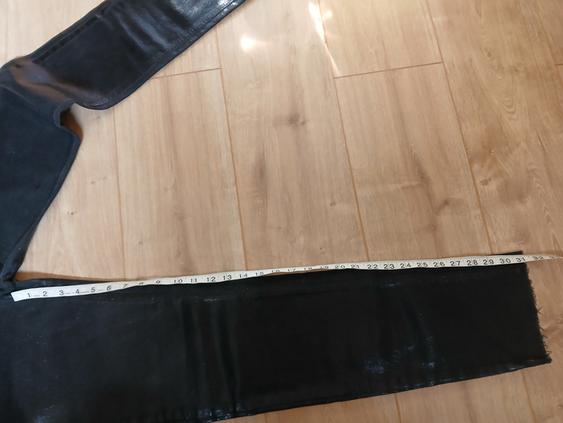 Black trousers on a light wooden floor, with a white tape measure measuring the length of the right leg.