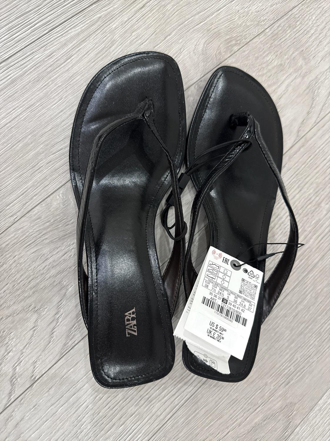 Pair of black sandals on a wooden floor. The insole reads ZARA. They have a label bearing the text US $59.90 and UK £35.99.