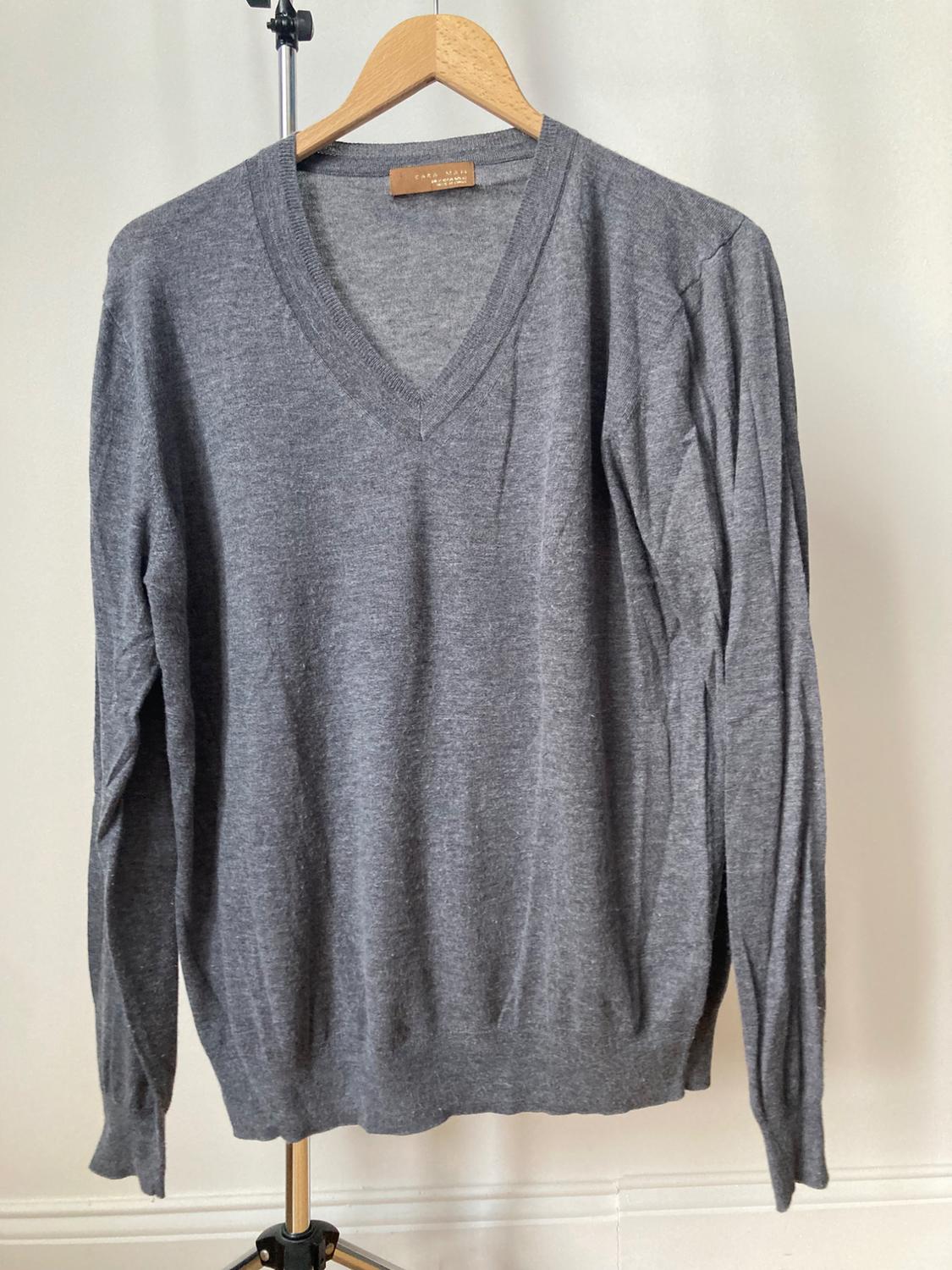 Front view of a grey V-neck, long-sleeved sweater hanging on a hanger.