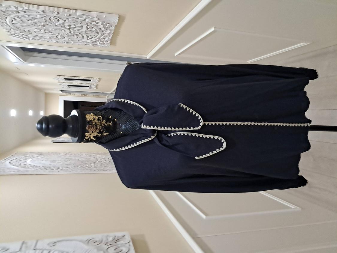 Mannequin in a black cape adorned with white trim and gold details on the collar, in a hallway with white wall decor.