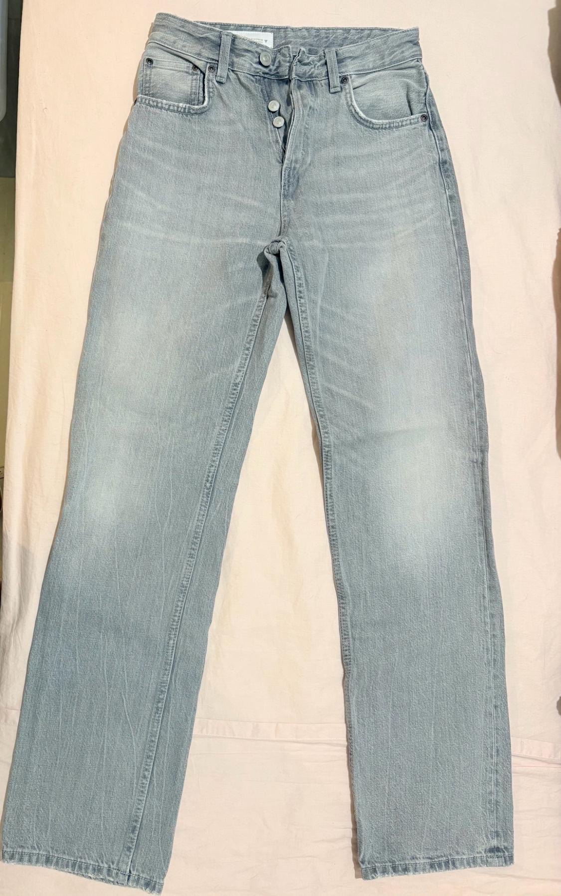 Light blue acid-wash denim jeans with button fastening, laid out on crinkled light pink fabric.