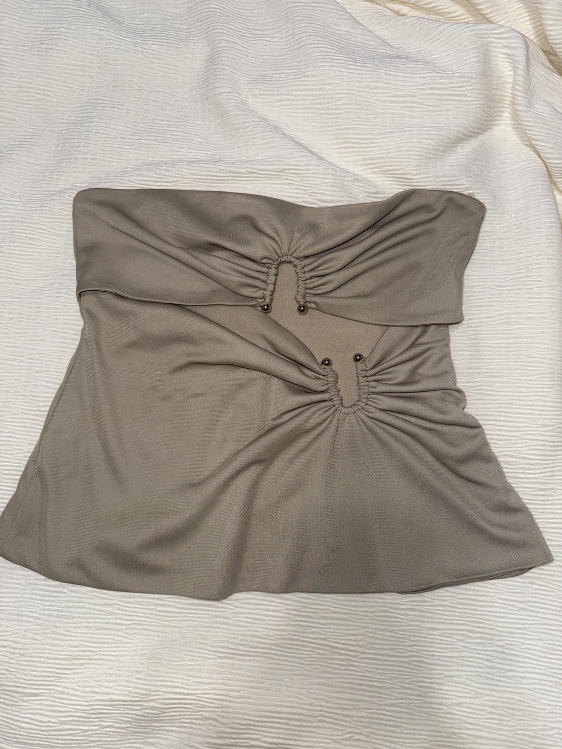 Beige strapless top with ruched detailing and bead embellishments, on textured white fabric.