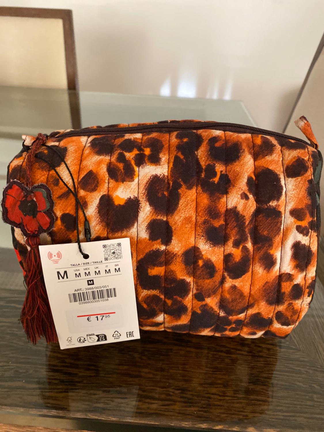Animal print handbag in orange and black tones on a glass table. Label shows size M and price €17.95.