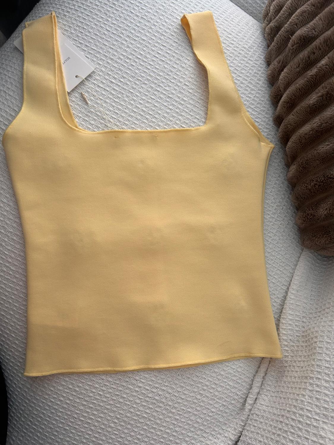 Yellow vest top on a textured white surface, with a visible label on the left-hand side.