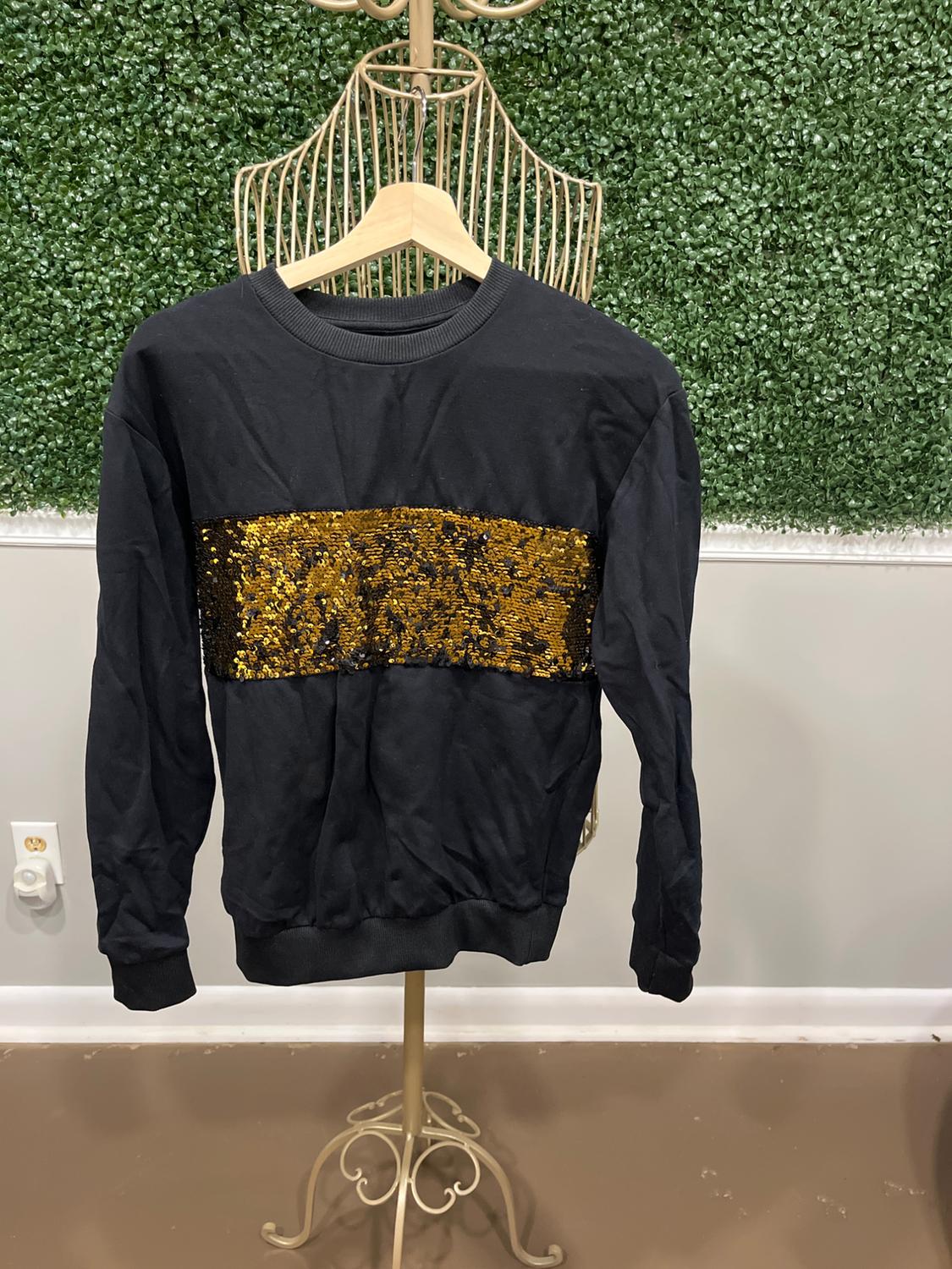 Black sweatshirt with a gold sequin stripe hanging on a metal mannequin, green leaf wall background.