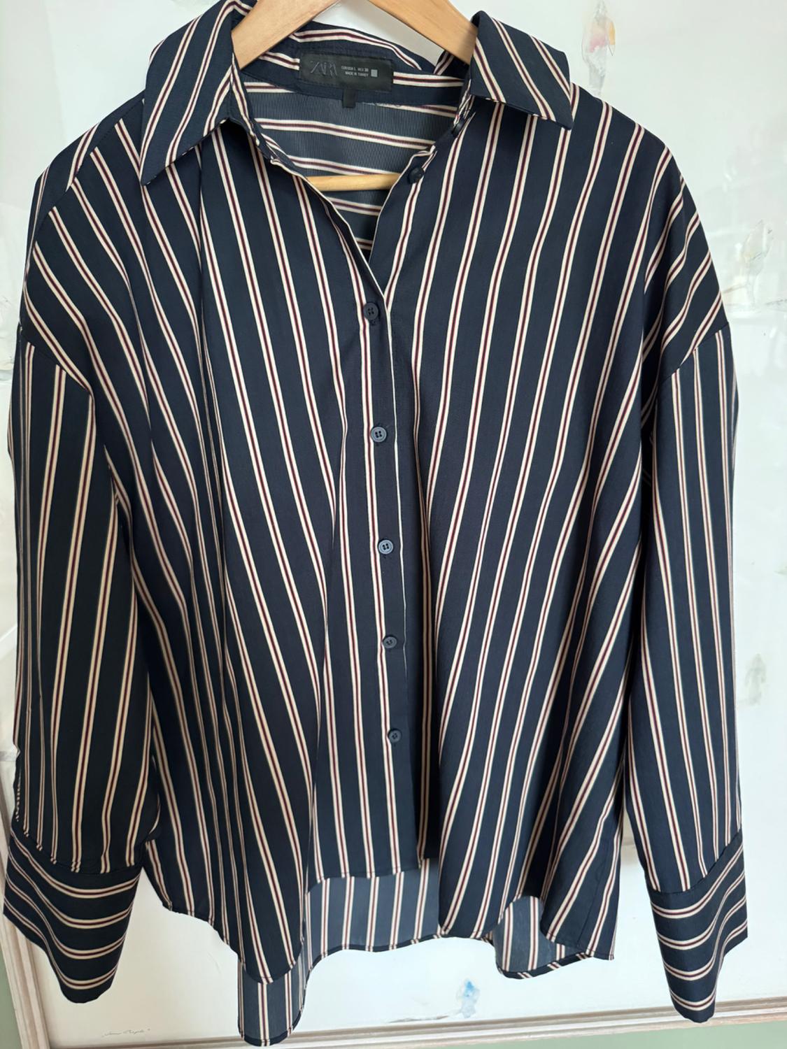 Navy blue long-sleeved ZARA shirt with red and white vertical stripes, button-down and hanging on a wooden hanger against a light background.