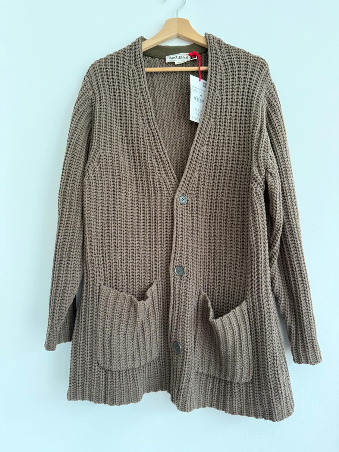 Brown knitted cardigan with buttons and large pockets, hanging on a wooden hanger. Visible label: "ZARA SRPLS".