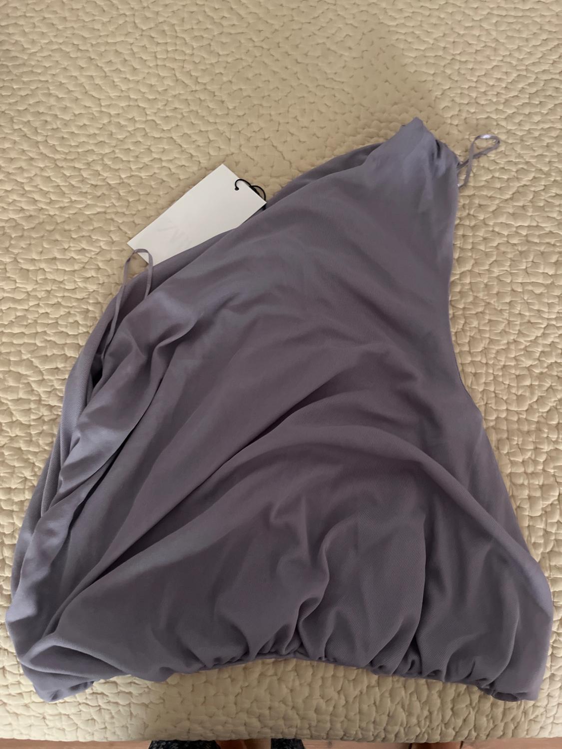 Lilac dress with thin straps on a beige bedspread, with a visible white label.