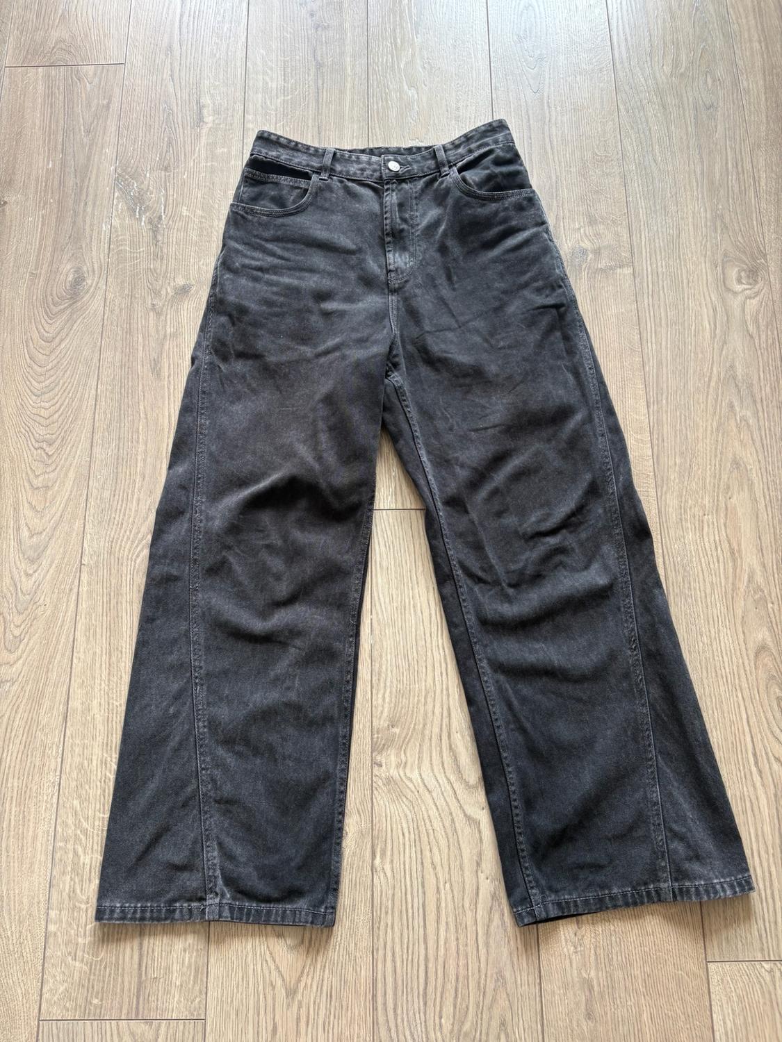 Dark grey wide-leg jeans with front seams, laid out on a light wood floor in a relaxed style.