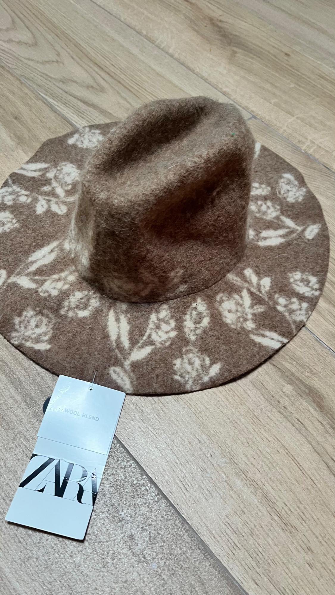 Brown hat with white floral print on a wooden floor. Visible label with text: "WOOL BLEND" and "ZARA".