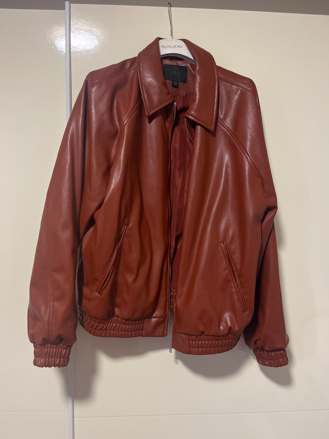 Brown jacket hanging on a white hanger with the label "reJouecation". Beige wall background.