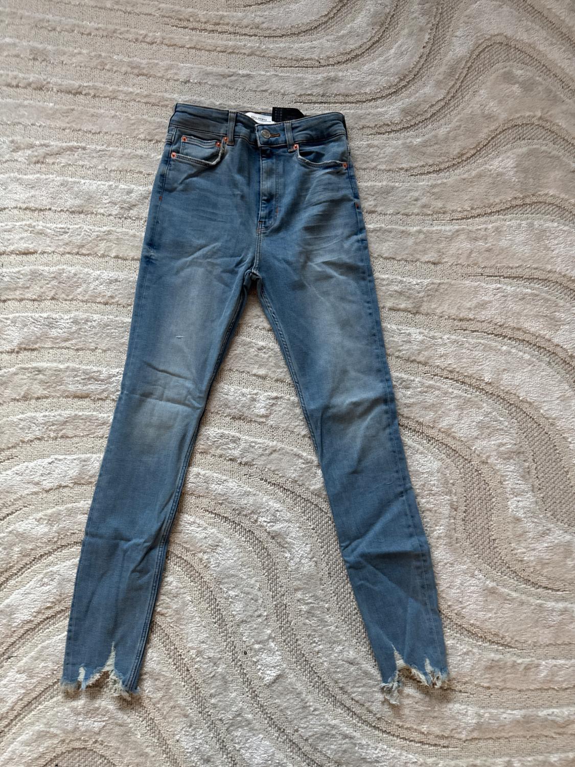 Front view of blue denim jeans with front pockets and a frayed hem.