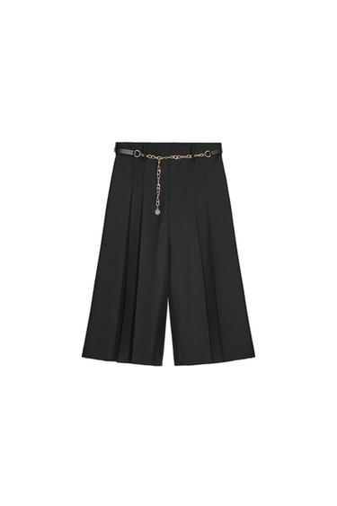 Front view of black pleated shorts with gold chain belt.