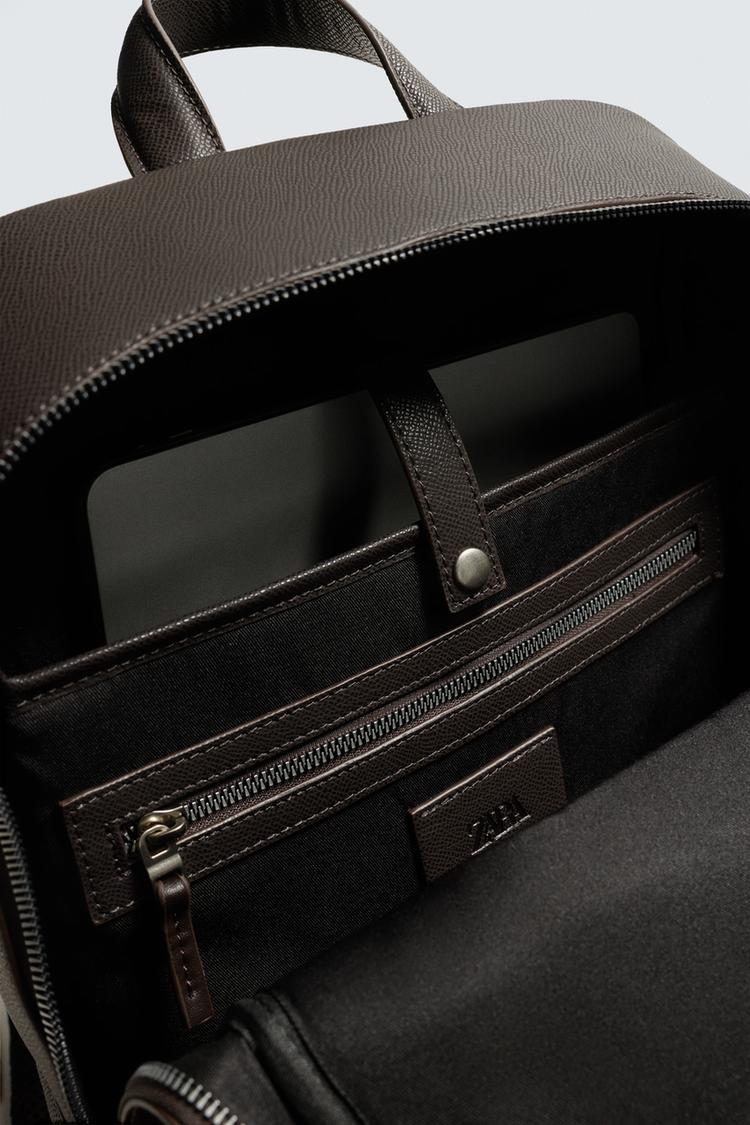 Detalhe do interior de uma mochila marrom com compartimento para dispositivos, bolso com zíper e alça superior.