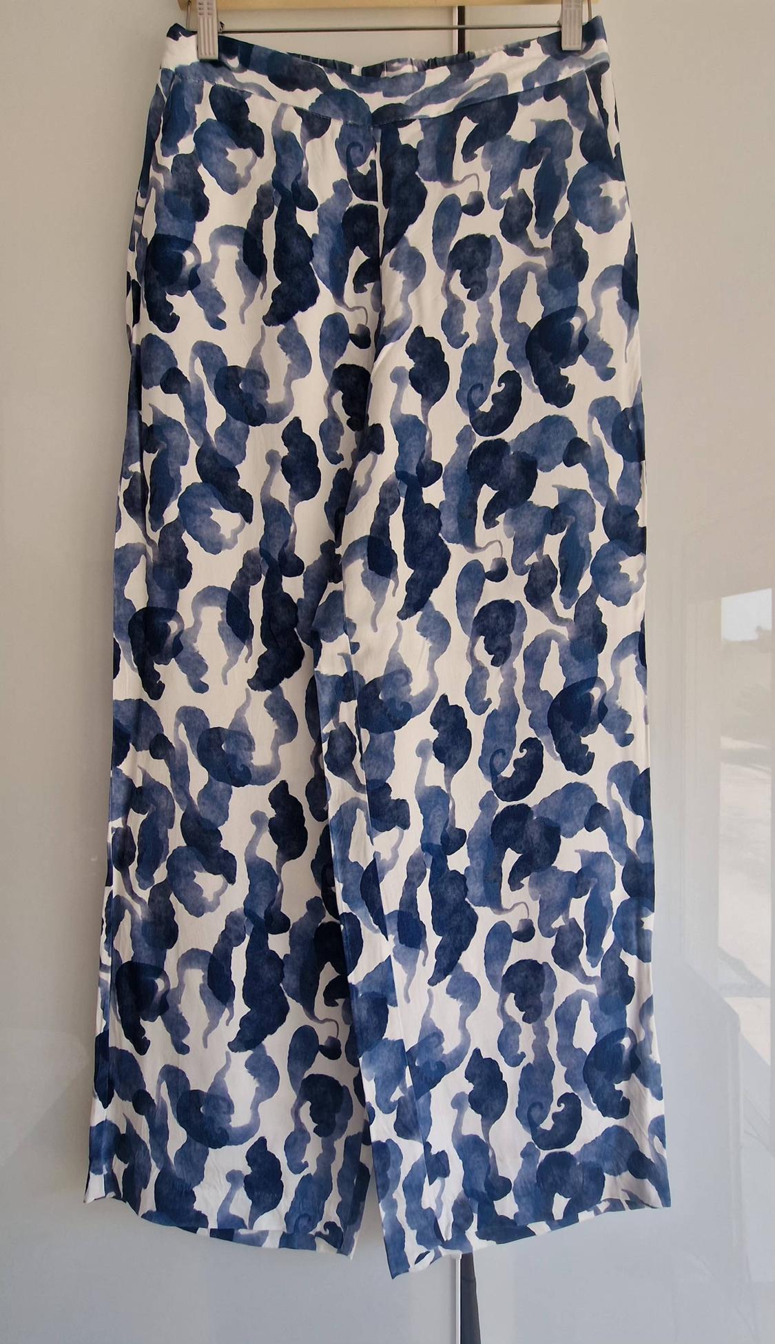 Flowing trousers with an abstract print in shades of blue and white, hanging on a hanger against a light background.