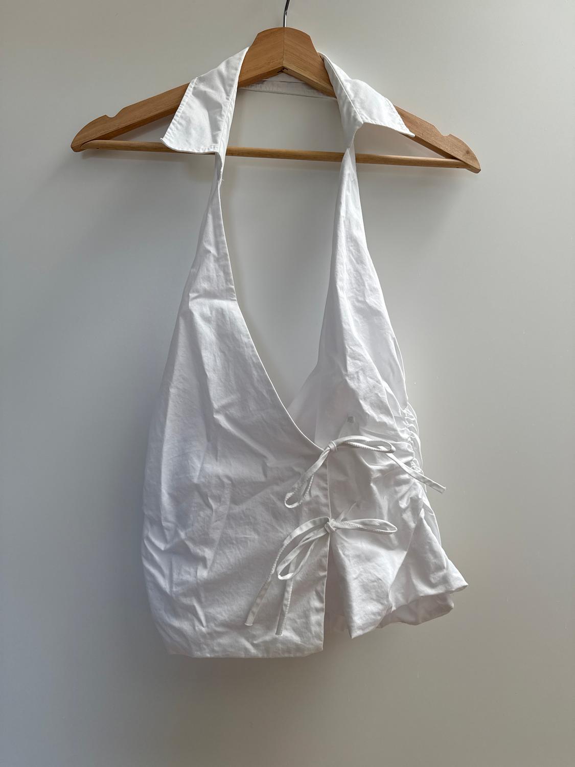 White sleeveless blouse with collar and ties at the front, hanging on a wooden hanger against a white background.