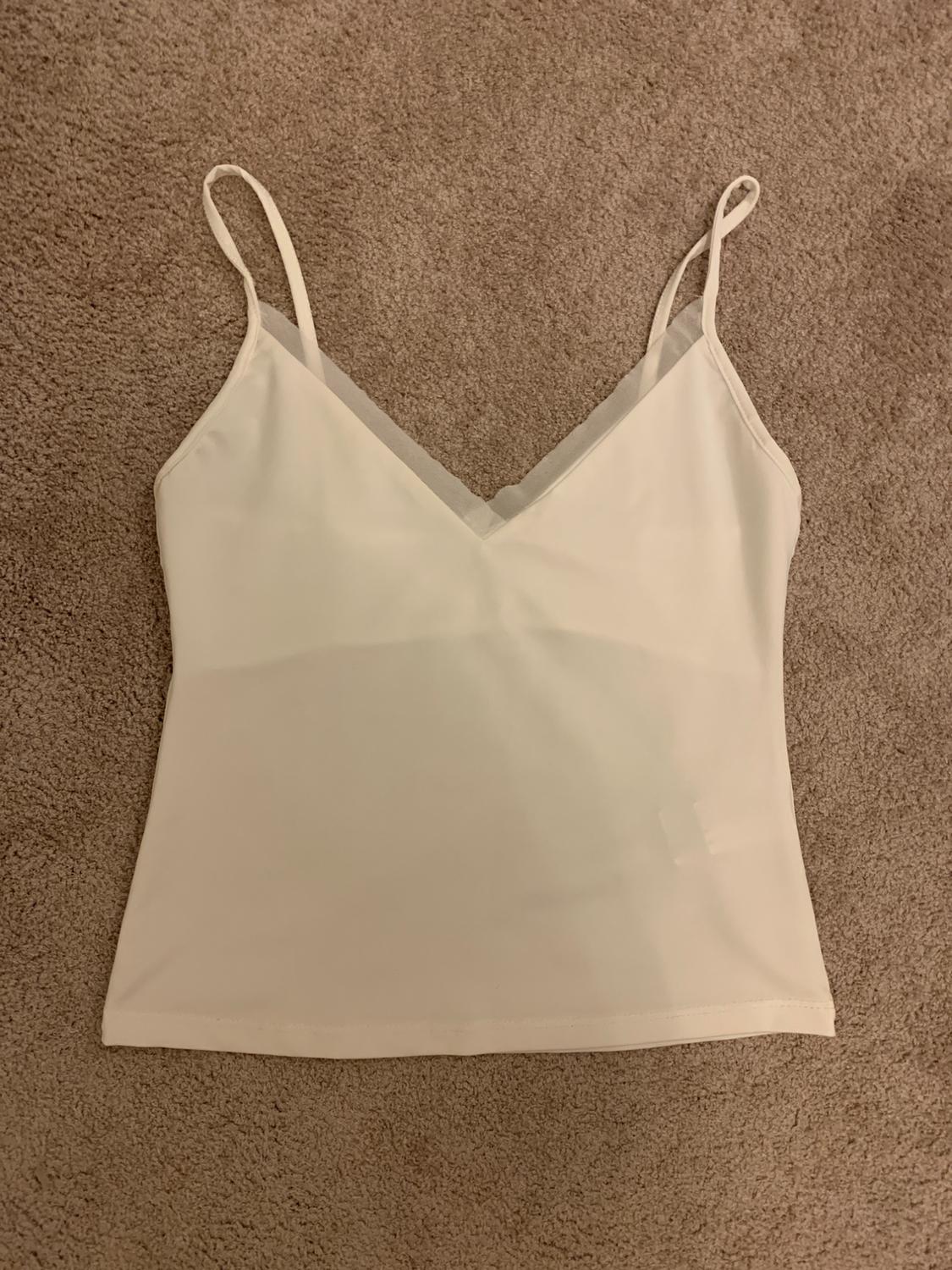 White vest top on a beige rug. Simple design with a V-neck and thin straps.