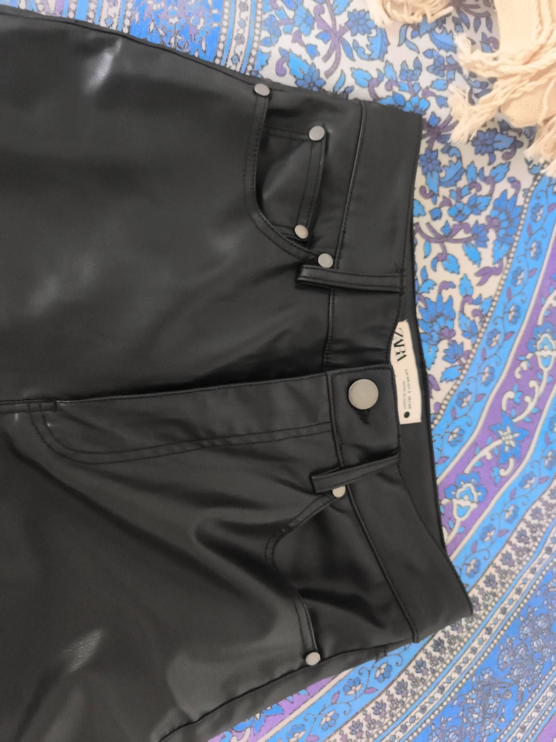 Black trousers with pockets and a silver button on a fabric patterned in blue and purple tones. Inner label bearing the text ZARA.