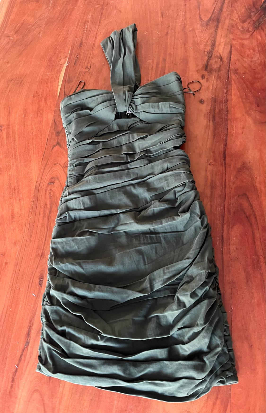 Olive green draped dress, with a single strap, on a brown wooden surface.