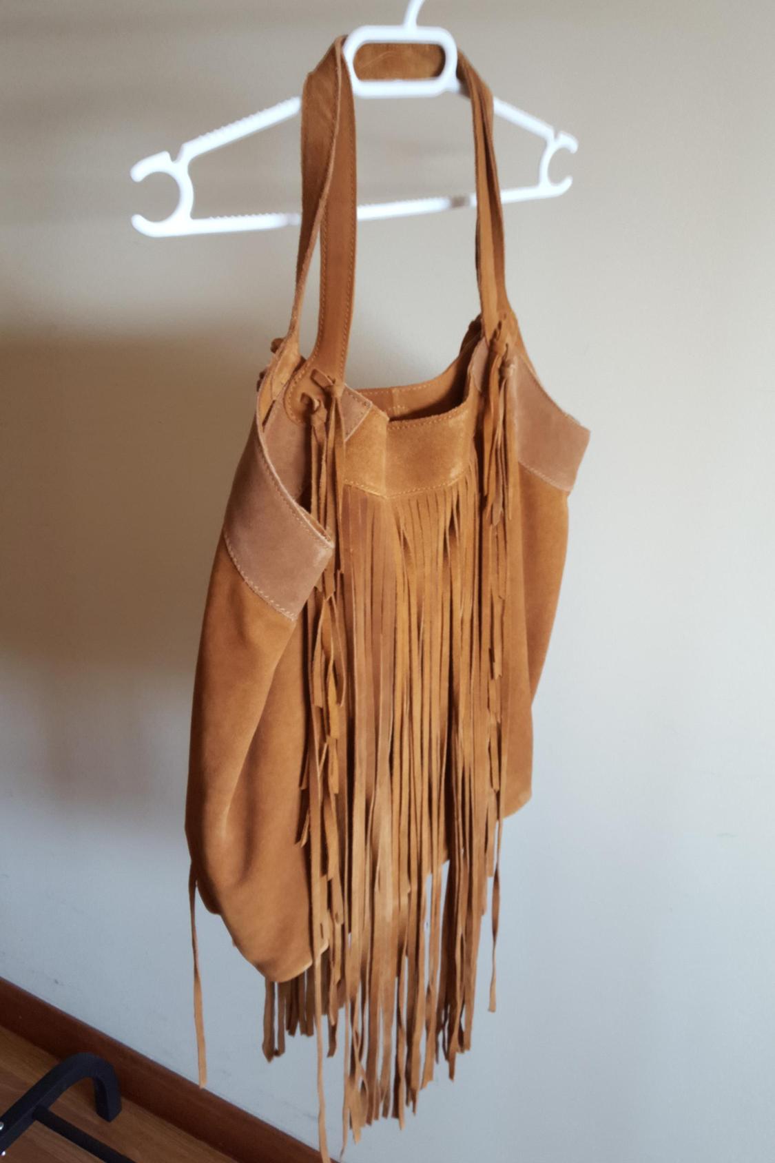 Brown handbag with long fringe hanging on a hanger.