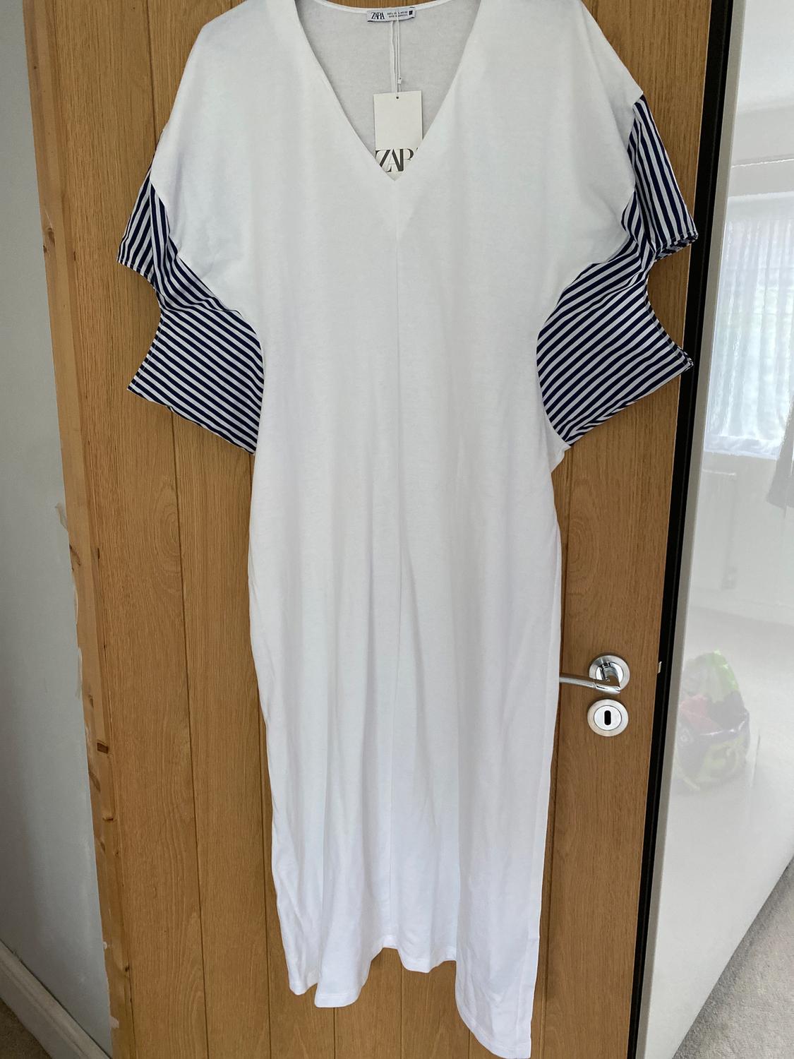 White dress with blue and white striped sleeves hanging on a wooden door. Visible label on the collar.