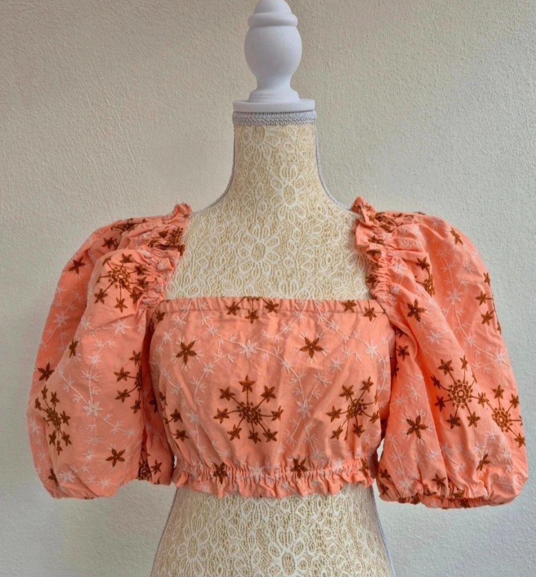 Peach-coloured crop top with puffed sleeves and brown embroidery, on a lace mannequin in front of a white wall.