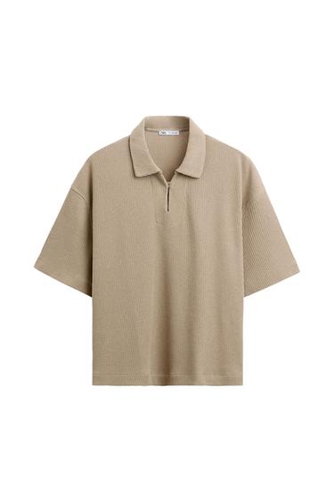 Beige knitted polo shirt with classic collar and short zip at the centre. Short sleeves and ribbed texture. White background.