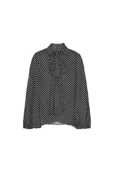 Front view of a black blouse with a white polka dot pattern and neck tie.