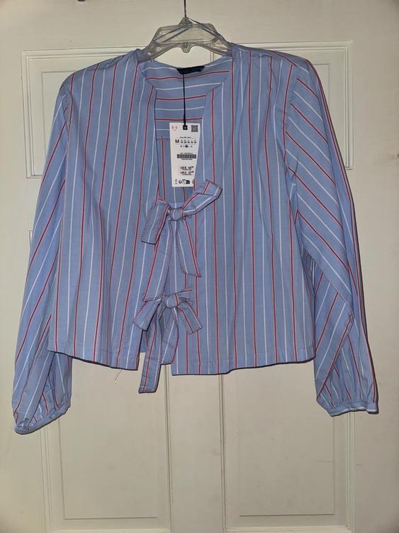 Blue and red striped blouse with a bow on the front, hanging on a clear hanger in front of a white door.