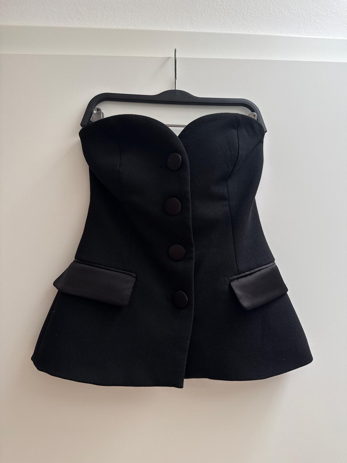 Black strapless top with large buttons and decorative pockets, hanging on a hanger against a white background.