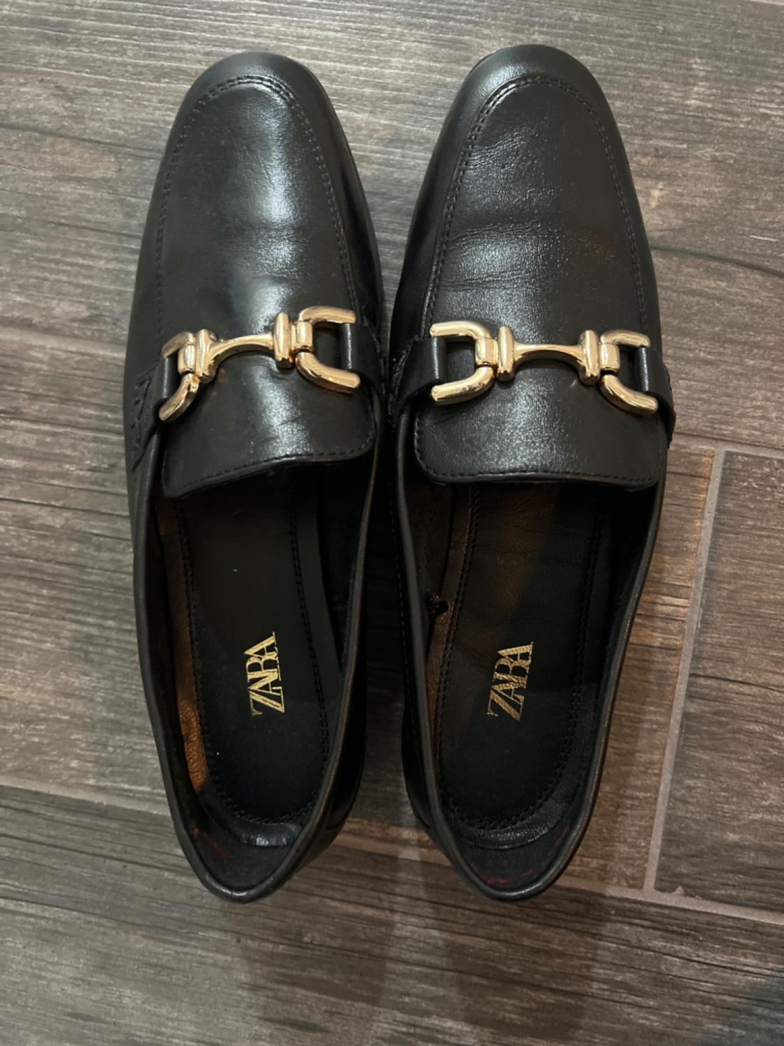 Top view of black loafers with gold metallic detail on the front.