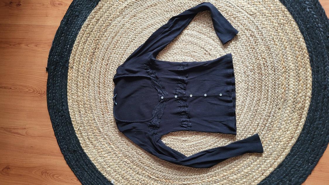 Black, long-sleeved jacket with buttons, placed on a round jute rug on a wooden floor.