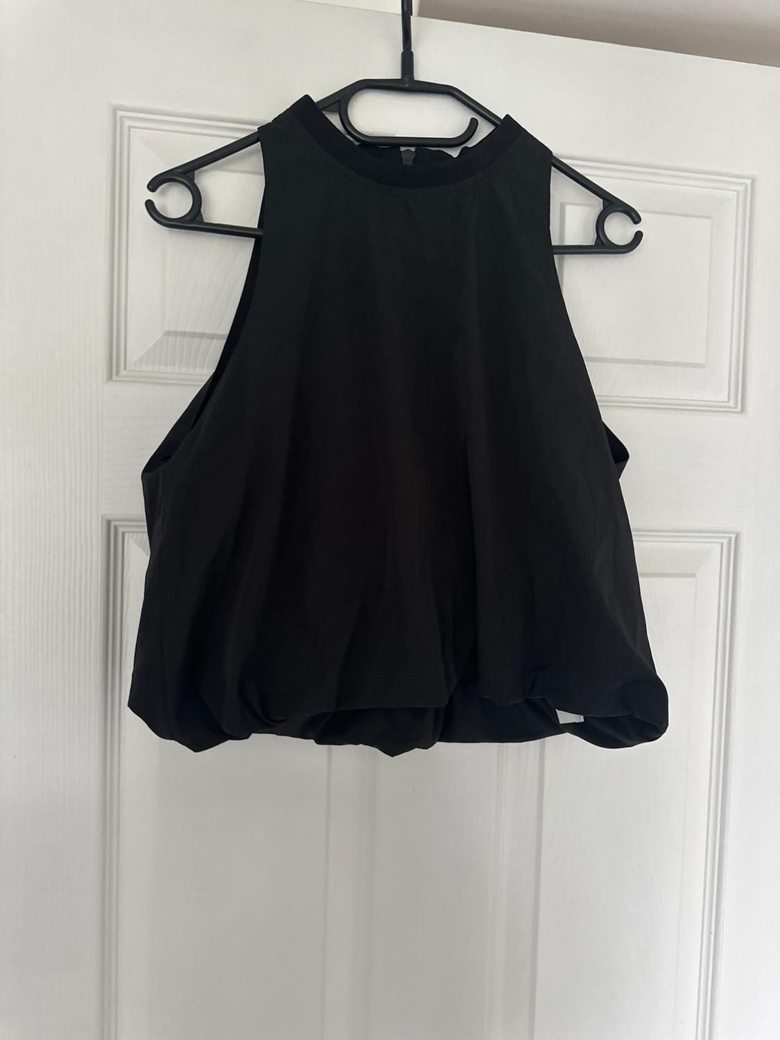 Black sleeveless top hanging on a black coat hanger over a white door.
