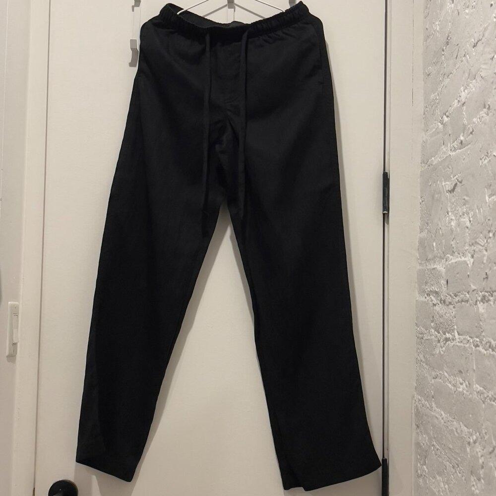 Black pants with an elastic waistband and drawstring, hanging from a white door.